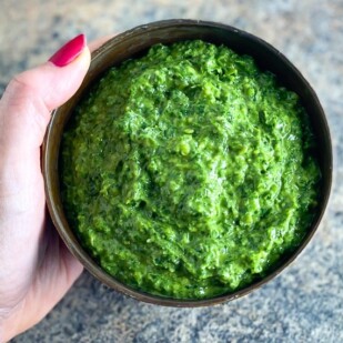 horizontal image of vegan low FODMAP kale pesto in a brown bowl, held by woman's manicured hand over stove surface