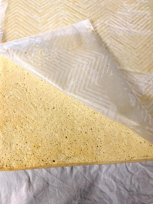 inverting sponge cake on linen towel, peeling back parchment paper