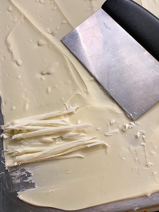 melted white chocolate spread onto back of sheet pan and allowed to firm up; using metal bench scraper to make white chocolate curls and shards