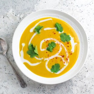overhead image of Vegan Low FODMAP summer Squash Soup with coconut milk swirled in; white bowl and silver spoon on grey speckled quartz surface
