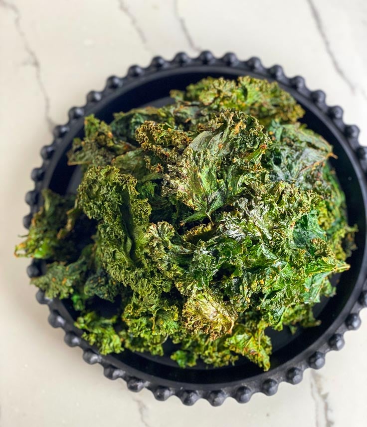 overhead image of kale chips piled up on black plate, white background
