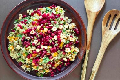 overhead image of low FODMAP Roasted Pumpkin and Quinoa salad with pomegranate seeds and nuts on brown ceramic plate