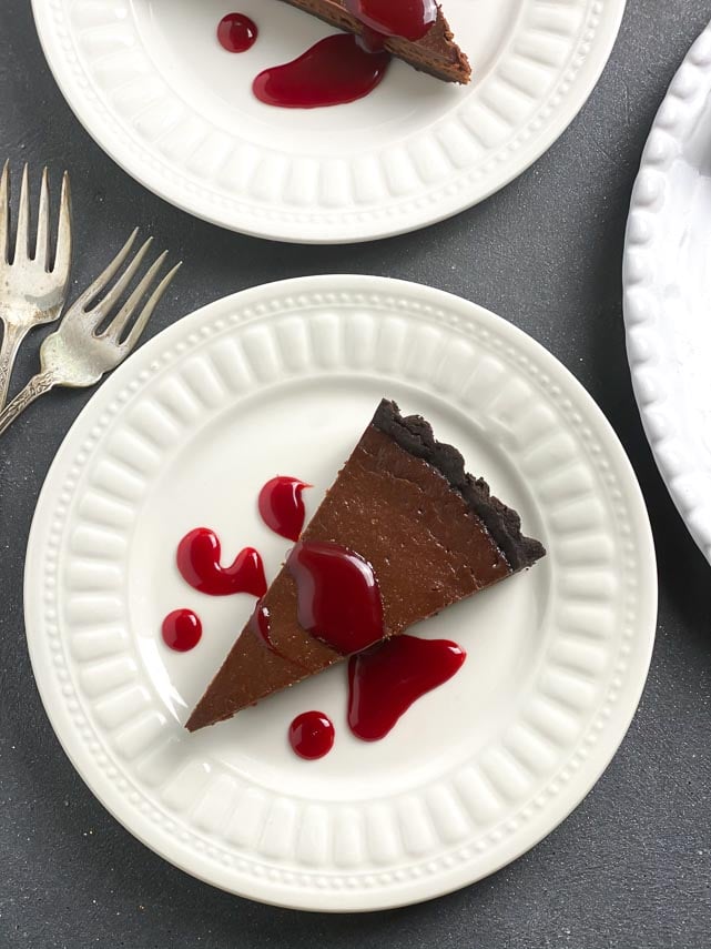 overhead image of wedge of chocolate tart with red caramel sauce on white plate; antique forks alongside