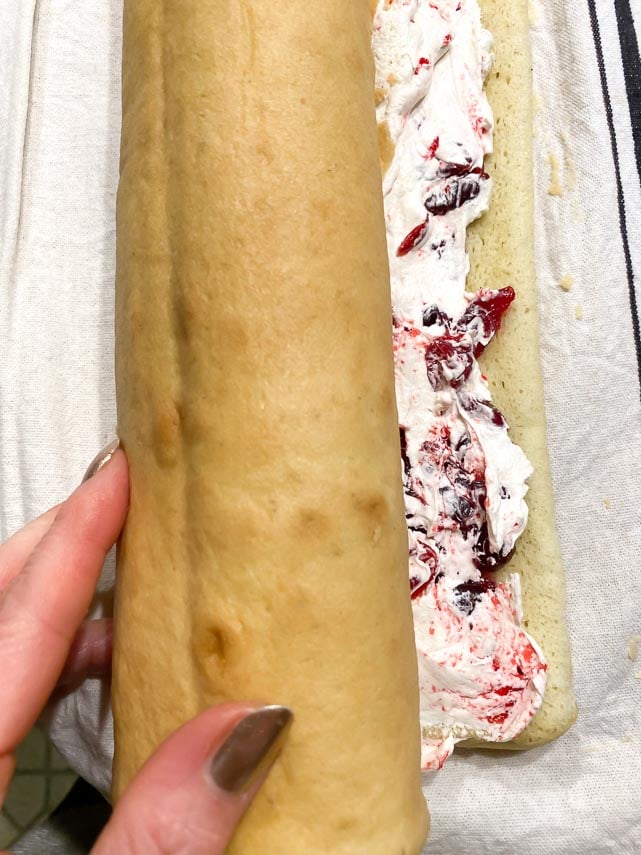 rolling up jellyroll cake with buttercream and cranberry filling