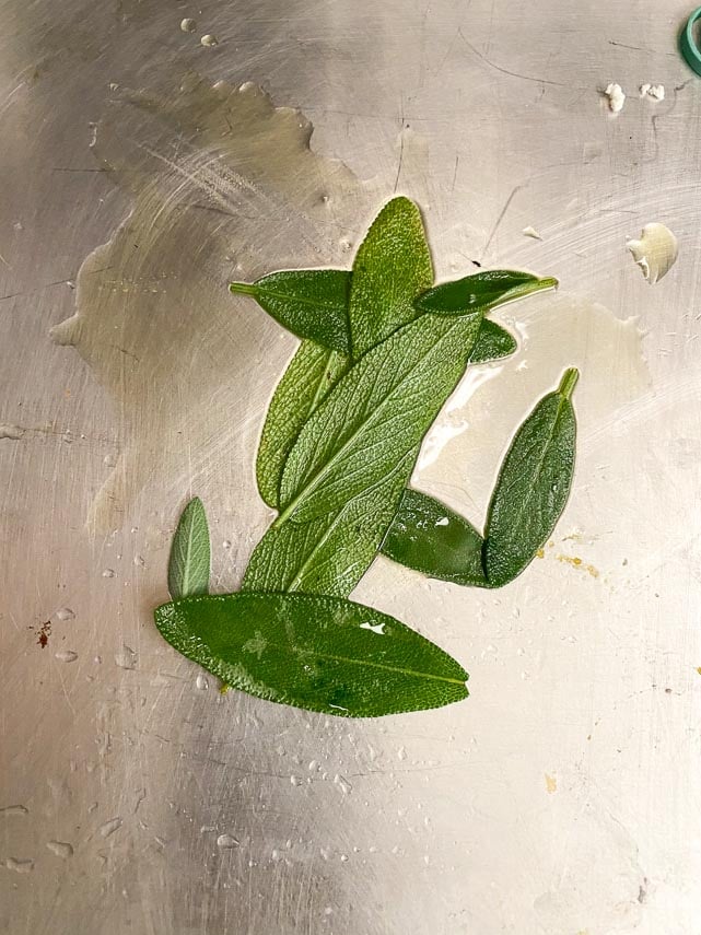 rubbing sage leaves with oil on stainless steel pan