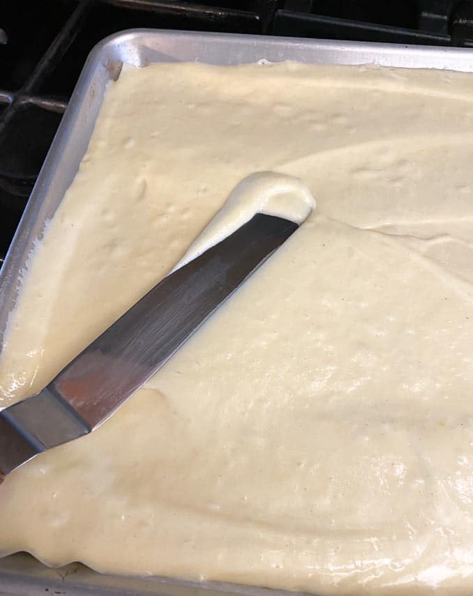 sponge cake batter being spread into jellyroll pan with offset spatula