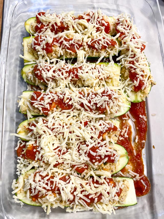 stuffed zucchini boats in baking dish, covered with toamo sauce and grated cheese