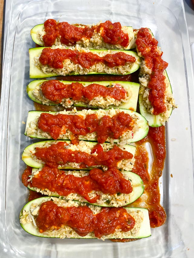 stuffed zucchini boats in baking dish, covered with tomato sauce