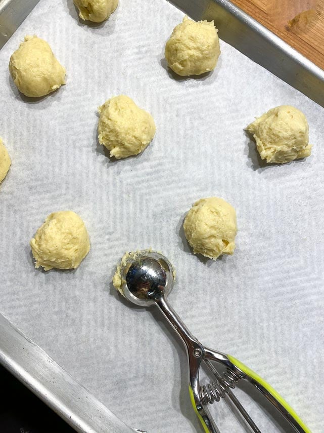 using a small scoop to dole out pate a choux on parchment lined pan