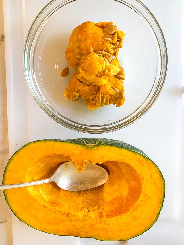 using a spoon to scoop out seeds from halved kabocha squash also known as Japanese pumpkin