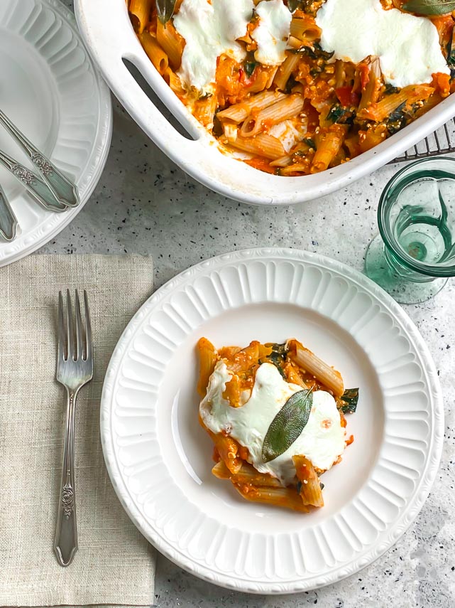 vertical image of baked pasta with roasted pumpkin, fresh mozzarella and sage on white plate