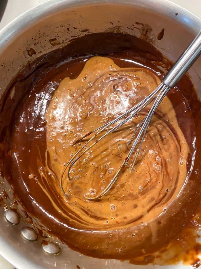 whisking tempered egg mixture into chocolate tart filling in pot with whisk