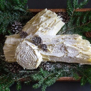 white chocolate buche de noel on wooden board with pine boughs