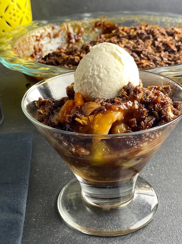 Low-FODMAP-Tropical-Crisp-in-a-glass-dish-with-chocolate-crisp-topping-dark-background-scoop-of-no-churn-vanilla-ice-cream