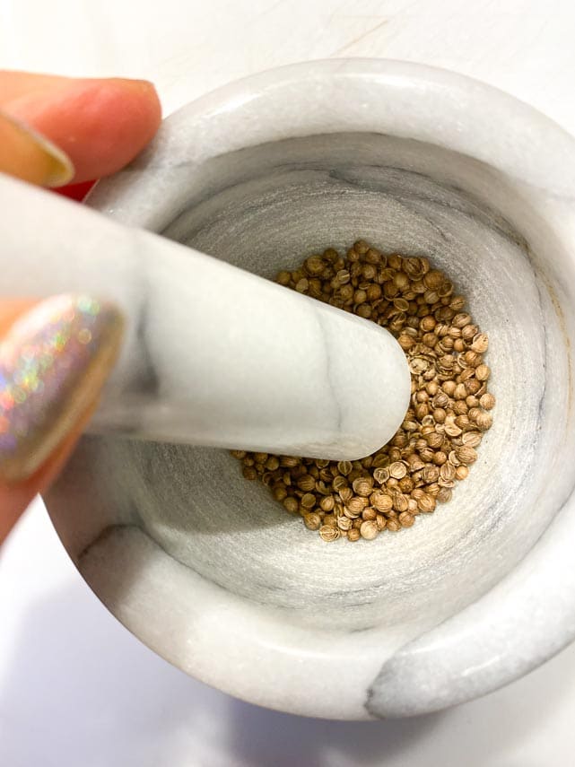 crushing coriander seeds in mortar and pestle