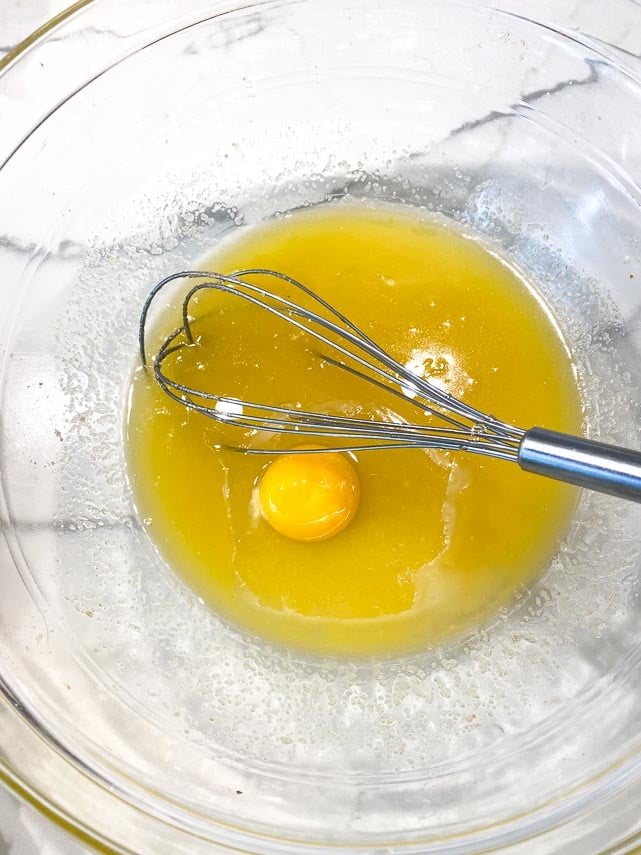 adding egg to melted butter and sugar in glass bowl