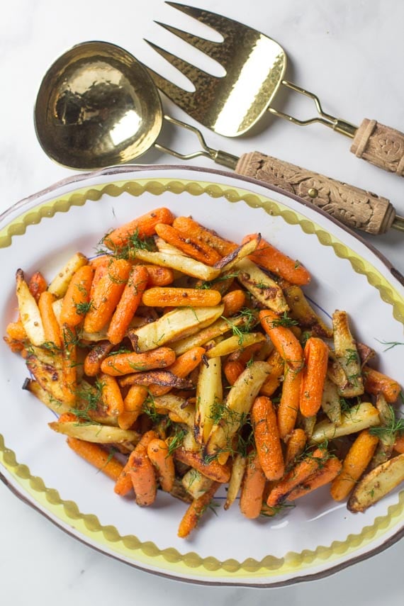 overhead of roasted carrots and parsnips on oval platter with brass serving pieces