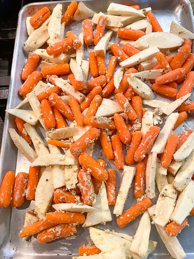 seasoned baby carrots and parsnips spread out on sheet pan