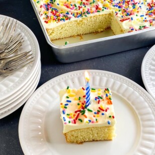 yellow-snack-cake-with-buttercream-rainbow-sprinkles-and-blue-candle-on-white-plate-1