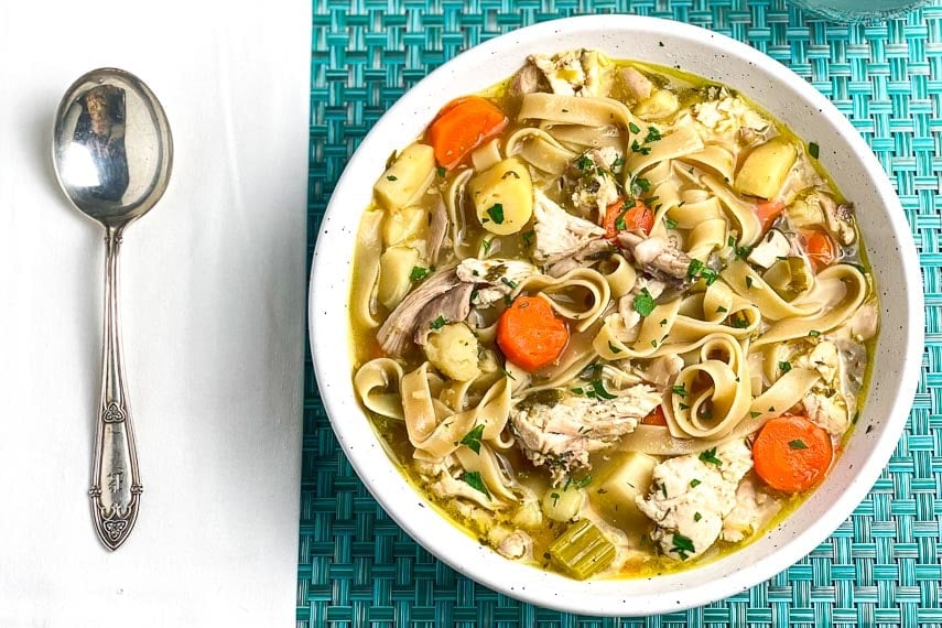 Low-FODMAP-Instant-Pot-Chicken-Noodle-Soup-with-Dill-in-white-bowl-on-aqua-placemat-and-silver-soup-spoon-white-napkin