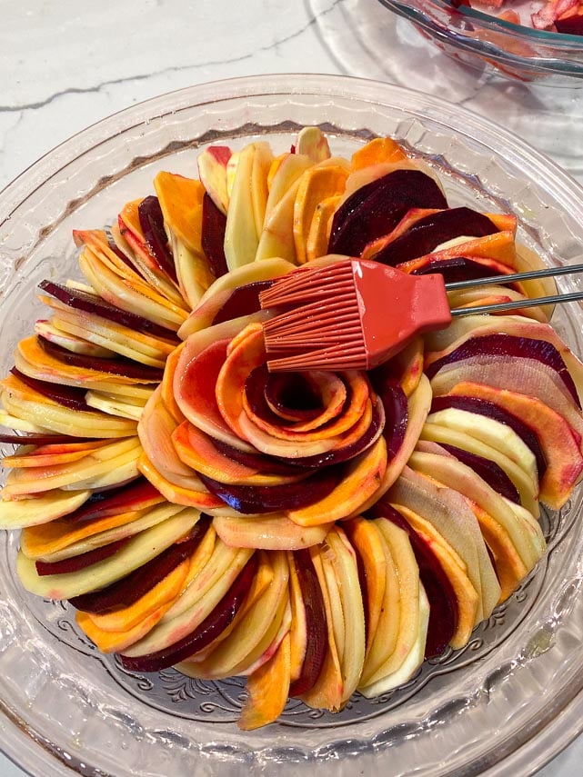 brushing-olive-oil-on-sliced-root-vegetables-layererd-in-a-glass-dish