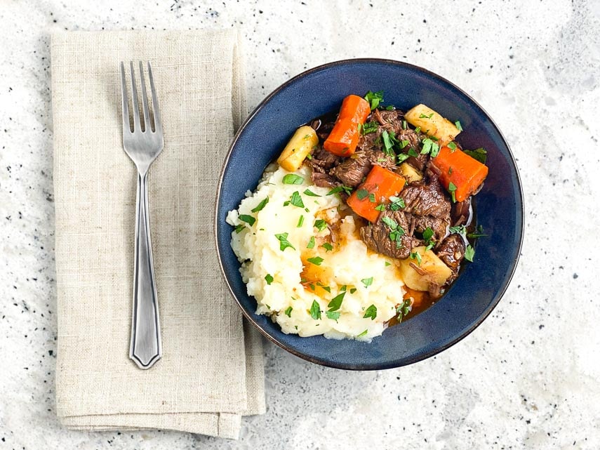 horizontal-overhead-image-of-Low-FODMAP-Instant-Pot-Beef-Stew-in-blue-bowl-on-gray-background