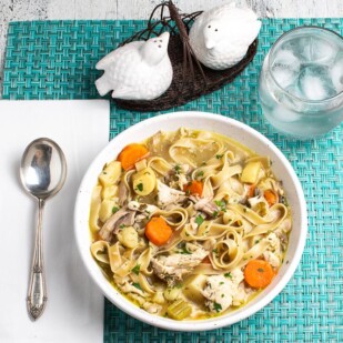 low-FODMAP-Instant-Pot-Chicken-Noodle-Soup-in-a-white-bowl-on-an-aqua-placemat-with-a-water-glass