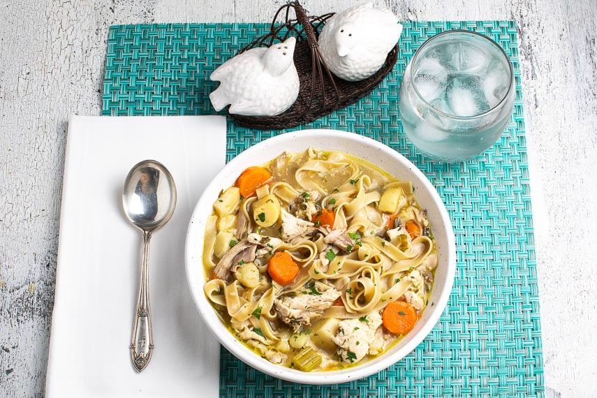 low-FODMAP-Instant-Pot-Chicken-Noodle-Soup-in-a-white-bowl-on-an-aqua-placemat-with-a-water-glass