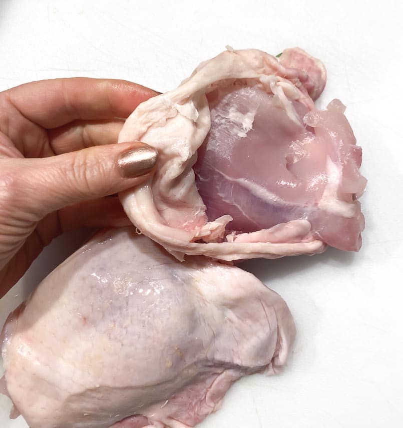 peeling-skin-off-of-a-chicken-thigh-on-a-white-surface