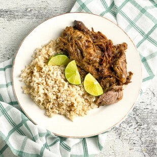 plated-low-FODMAP-Instant-Pot-Cuban-Style-Pork-on-white-plate-with-brown-rice-and-limes-white-painted-wood-background