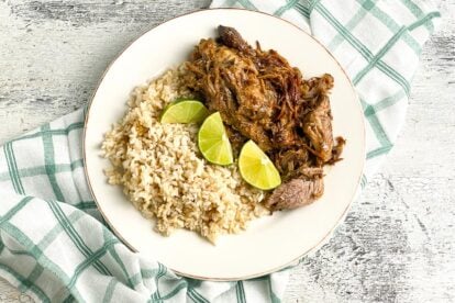 plated-low-FODMAP-Instant-Pot-Cuban-Style-Pork-on-white-plate-with-brown-rice-and-limes-white-painted-wood-background