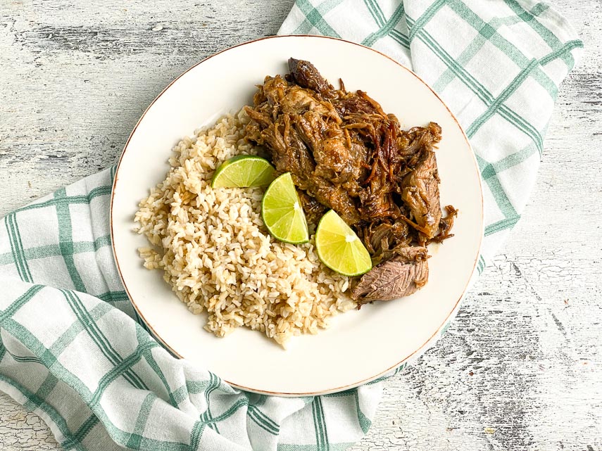 plated-low-FODMAP-Instant-Pot-Cuban-Style-Pork-on-white-plate-with-brown-rice-and-limes-white-painted-wood-background