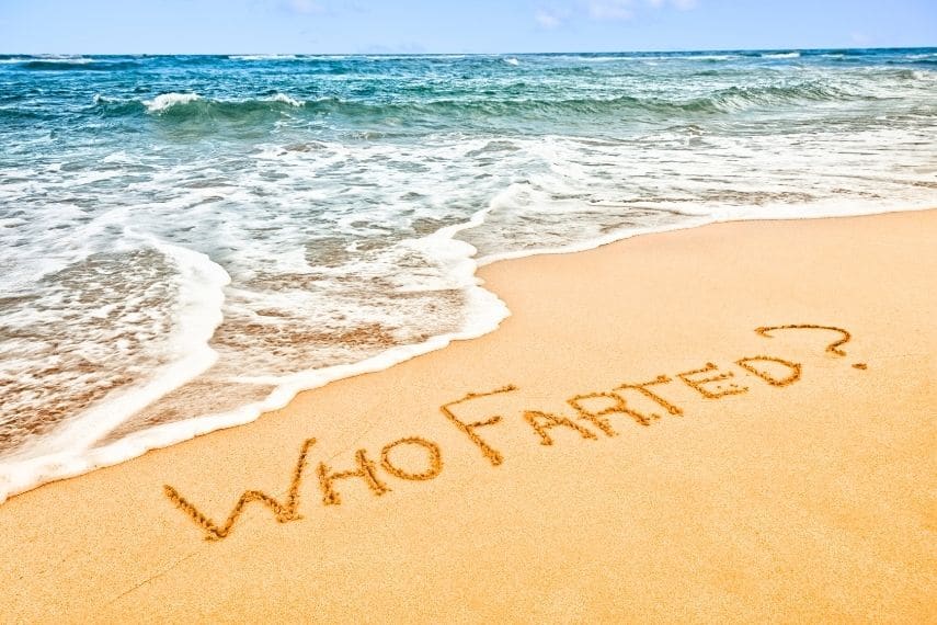 The words "Who Farted" written into the sand on a beach at the water's edge.