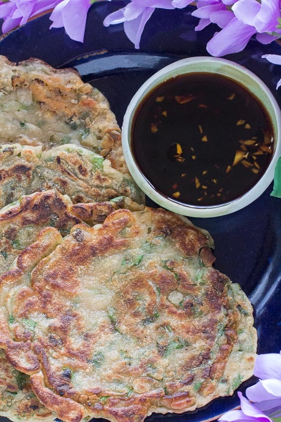 Low-FODMAP-scallion-pancakes-on-dark-plate-with-dark-background-with-dipping-sauce-and-purple-flowers-closeup