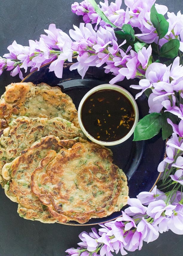 Low-FODMAP-scallion-pancakes-on-dark-plate-with-dark-background-with-dipping-sauce-and-purple-flowers