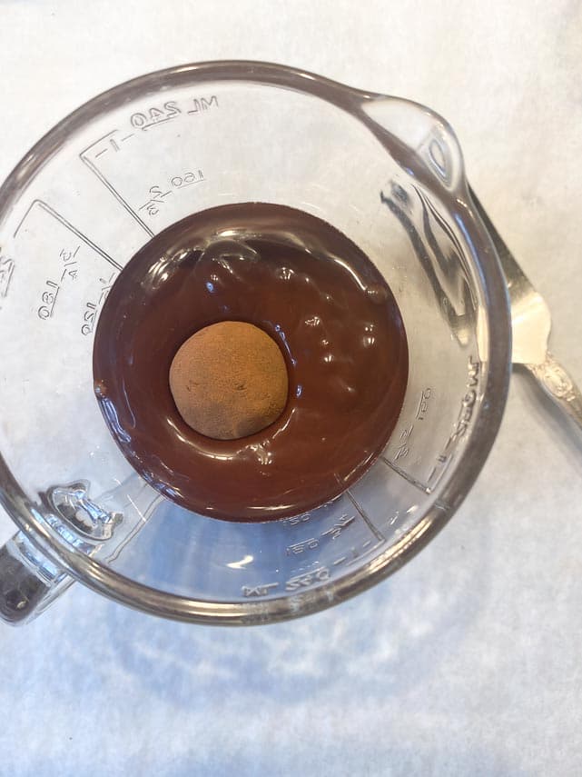 dropping truffle center in tempered chocolate in glass measuting cup
