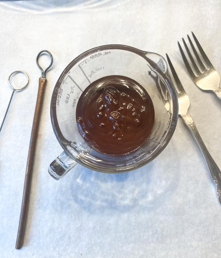 melted chocolate in a glass measuring cup with chocolate confectionery dipping tools alongside