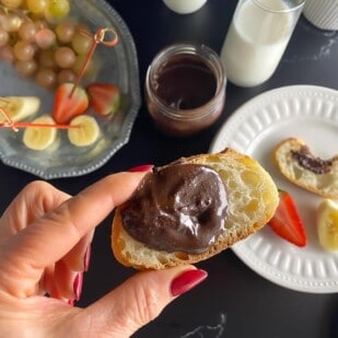 horizontal image on Low FODMAP Nutella on bread held in manicured hand against dark background