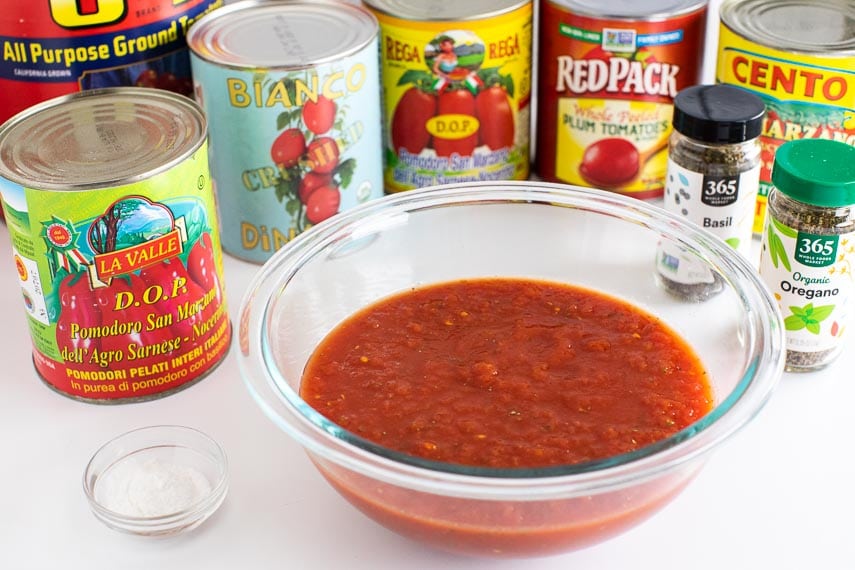 low FODMAP Pizza Sauce in glass bowl with cans of tomato products on white background