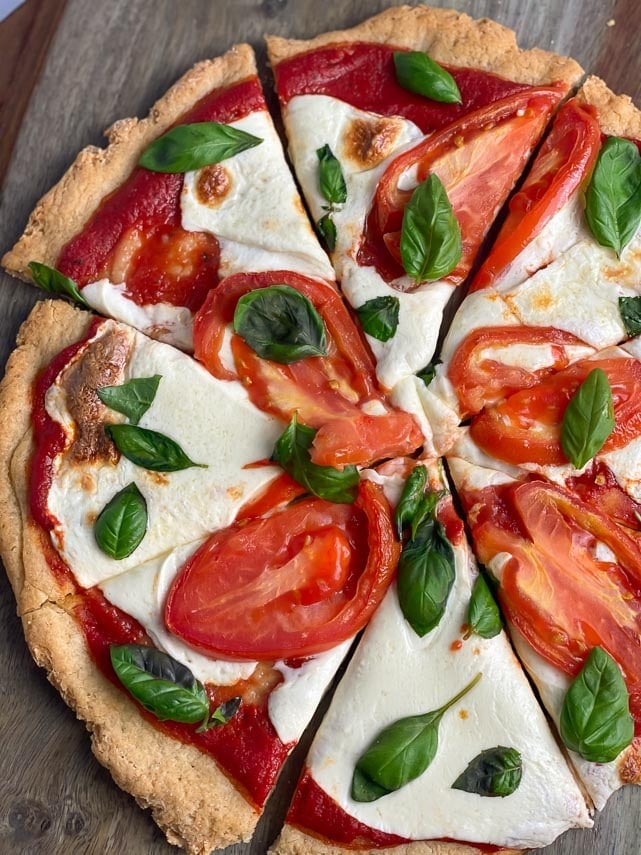 pizza with fresh mozzarella, tomatoes and basil, cut into wedges, on wooden board