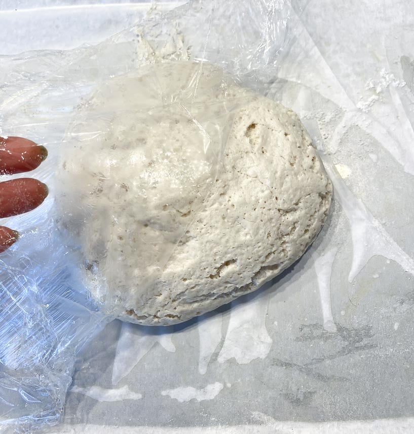 plastic wrap being removed from ball of risen pizza dough