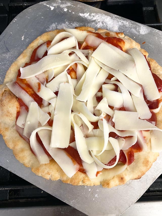 using metal pizza peel to remove par-naked pizza dfrom oven, sauce and cheese applied