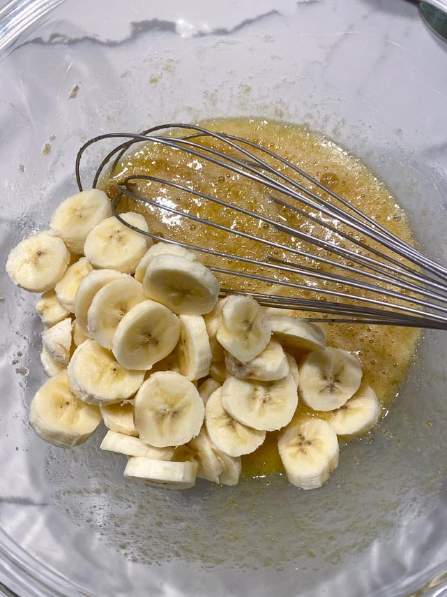 adding soft bananas to wet mixture to make banana bread in glass bowl