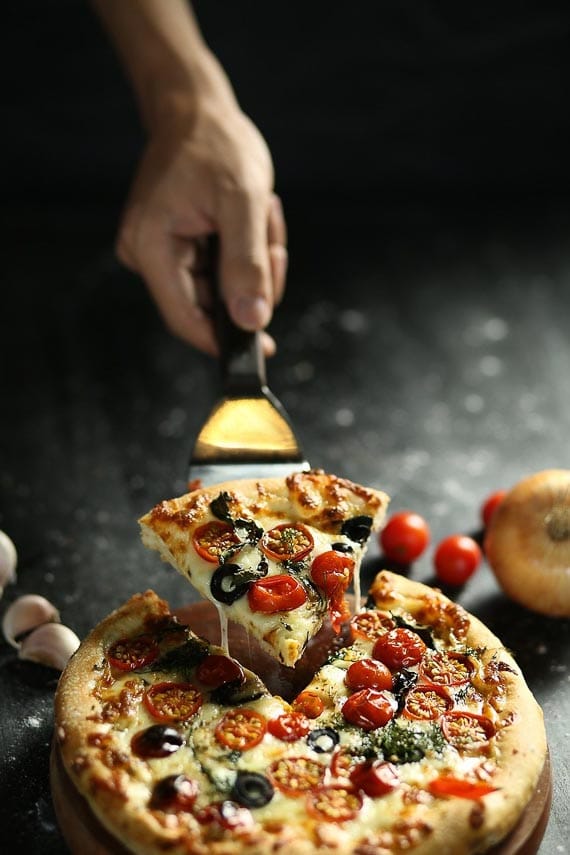 man serving a wedge of pizza on a dark background