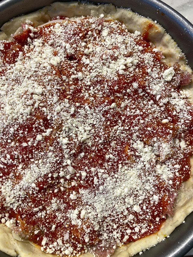 parmesan cheese sprinkled on top of deep dish pizza, before baking
