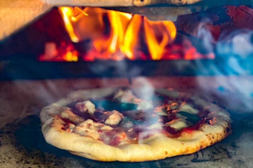 Main image of wood fired pizza in oven with live flames