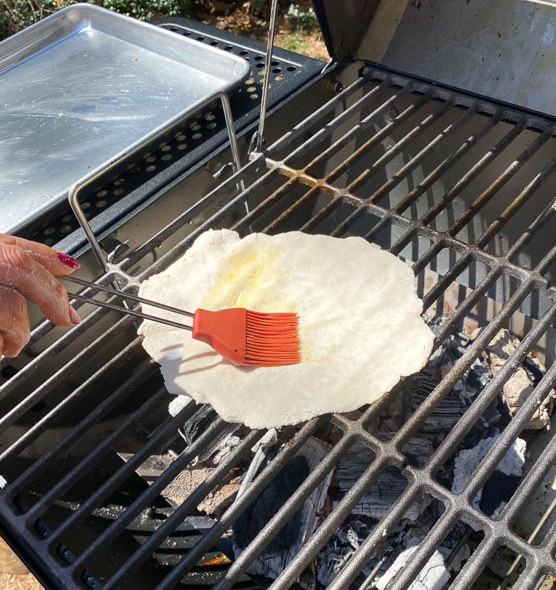 brushing grilled pizza dough with olive oil on grill