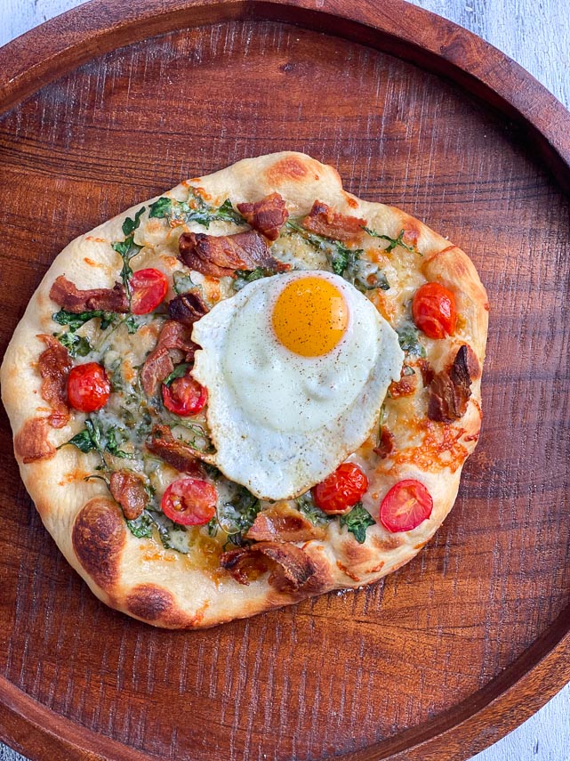 closeup of breakfast pizza with an egg on a wooden round tray