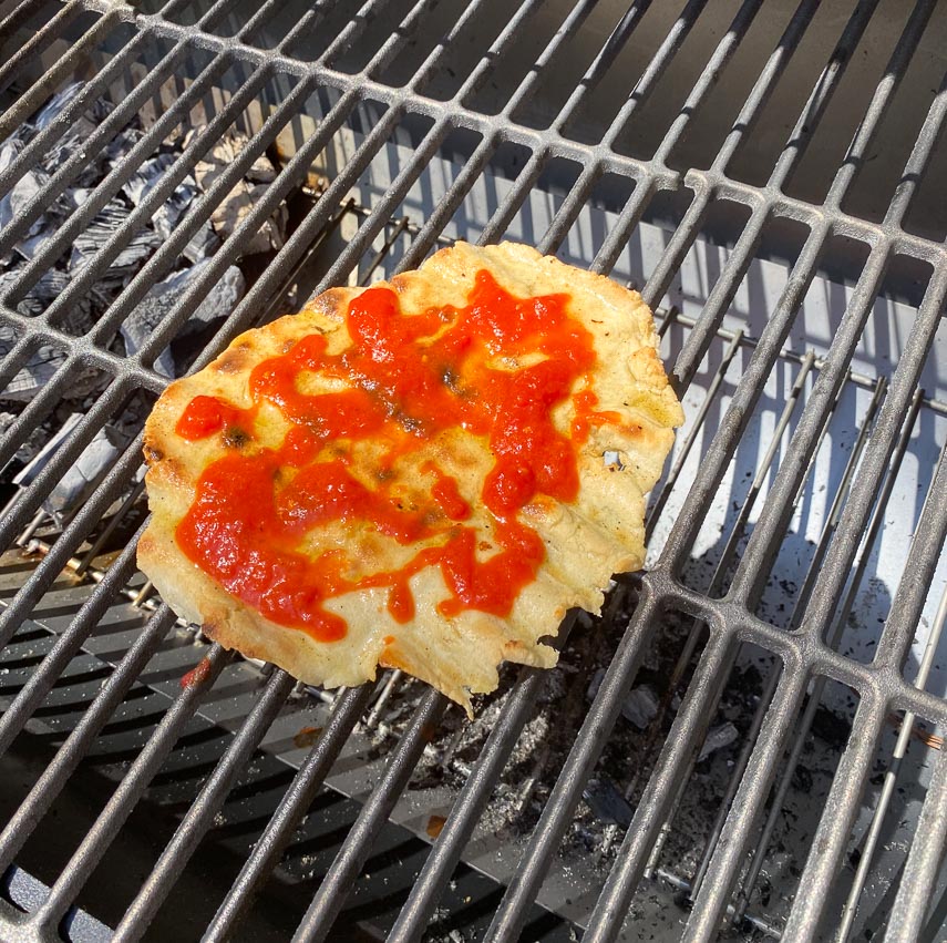 grilled pizza dolloped with tomato sauce on grill