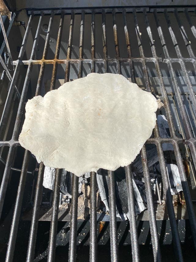 grilled pizza dough placed on hot side of grill